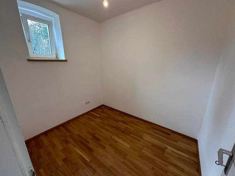 Kompaktes Zimmer mit dunklem Holzfußboden und einem Fenster mit Blick ins Freie.