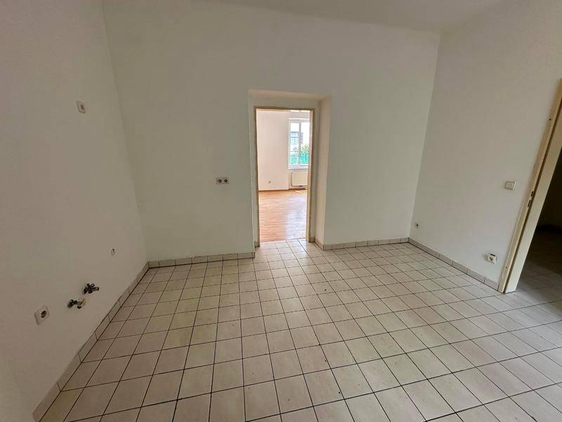 Unmöblierte Küche mit Fliesenboden und Anschlüssen für Spüle und Geräte.