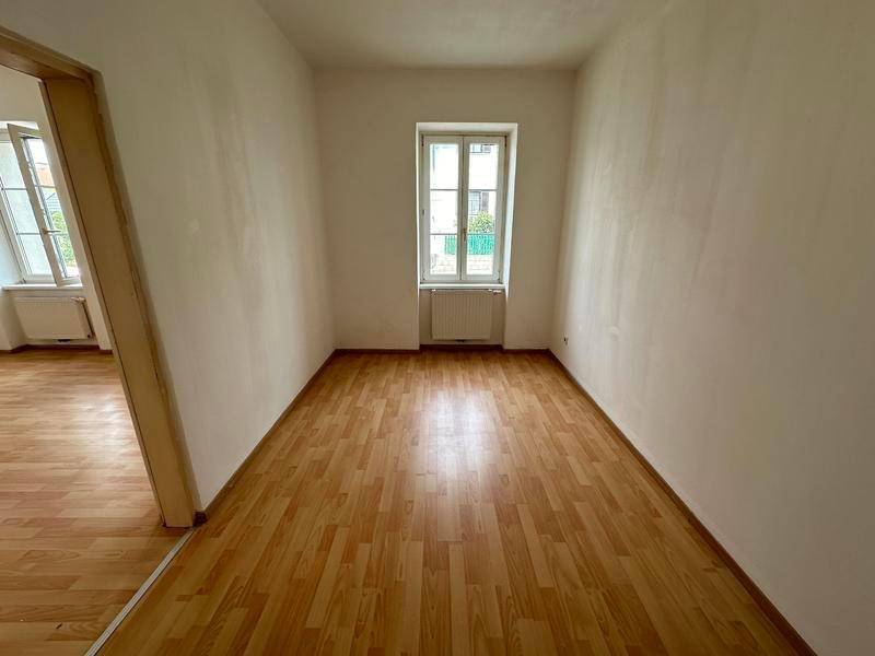 Schmaler Raum mit Laminatboden und einem Fenster, das den Blick nach draußen freigibt.