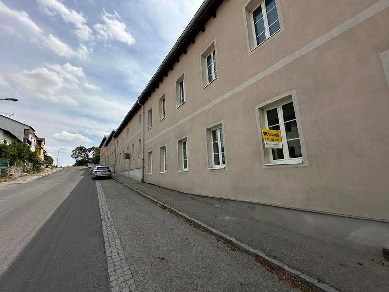 Lange Gebäudefassade entlang einer Straße mit mehreren Fenstern und einem "Wohnung zu vermieten"-Schild.
