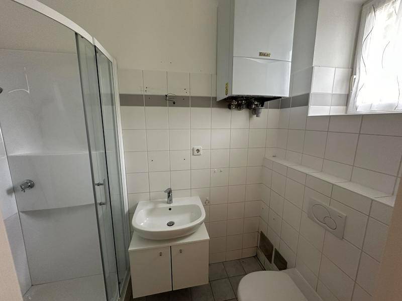 Funktionales Badezimmer mit Duschkabine, Waschbecken, WC und Warmwasserbereiter.