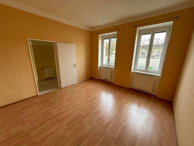 Helles Zimmer mit gelben Wänden und Laminatboden, mit Zugang zu einem weiteren Raum.