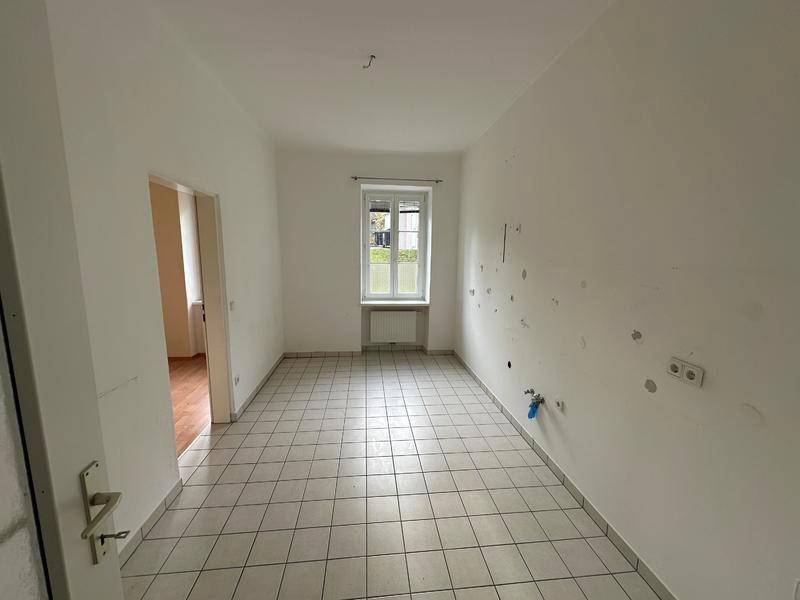 Leerer Küchenraum mit Fliesenboden und Anschlüssen, bereit für die Installation einer Einbauküche.