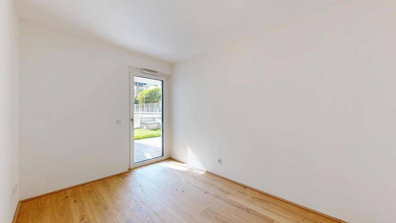 Helles Schlafzimmer mit Holzboden und Fenstertür, die zum Außenbereich führt.