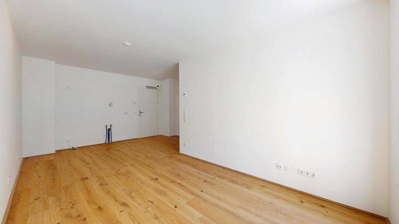 Leerer Küchenbereich mit Anschlüssen für eine moderne Einbauküche und Parkettboden.