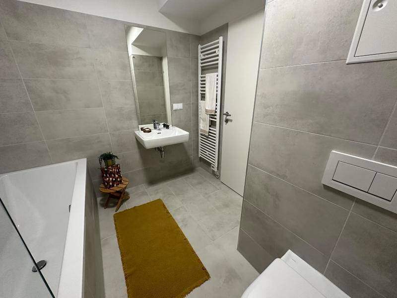 Badezimmer mit grauen Fliesen, Einzelwaschbecken, Spiegel und beheiztem Handtuchhalter.