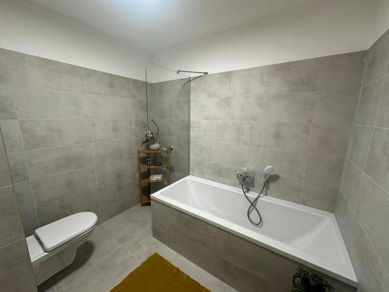 Modernes Badezimmer mit grauen Fliesen, Badewanne und wandhängendem WC.