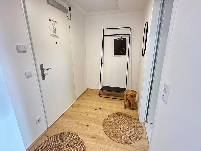 Heller Eingangsbereich mit Holzboden, Garderobe und dekorativen runden Teppichen.
