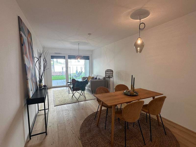 Essbereich mit Holztisch und Stühlen, im Hintergrund der Wohnbereich mit Zugang zur Terrasse.