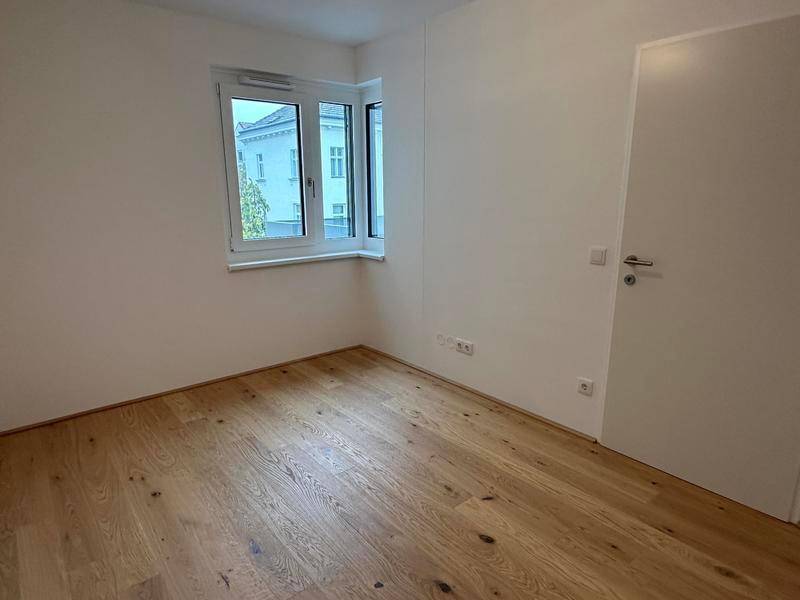 Helles Schlafzimmer mit Parkettboden und einem Fenster, das viel Tageslicht hereinlässt.