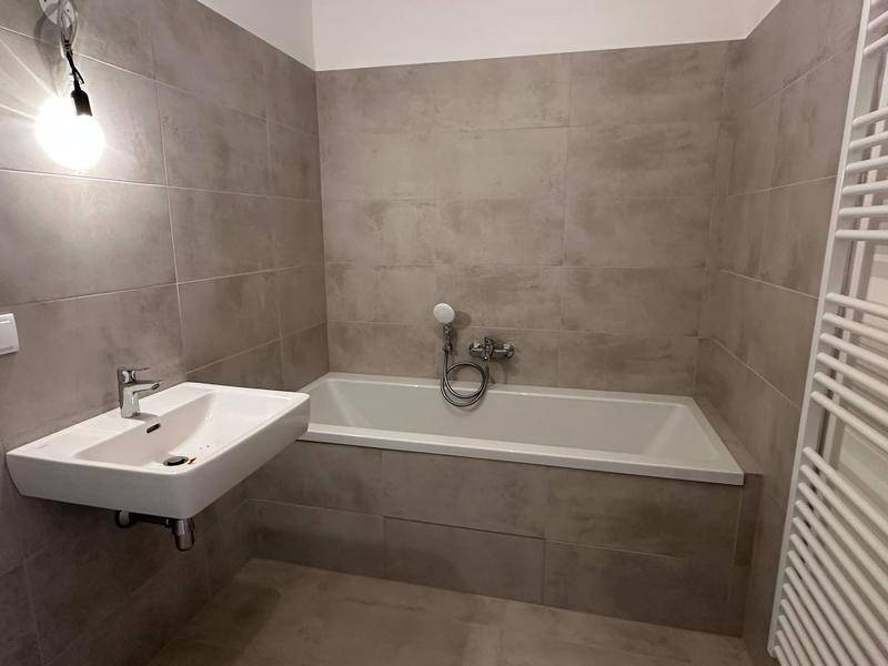 Modernes Badezimmer mit Badewanne, Einzelwaschbecken und grauen Fliesen, inklusive Handtuchheizkörper.