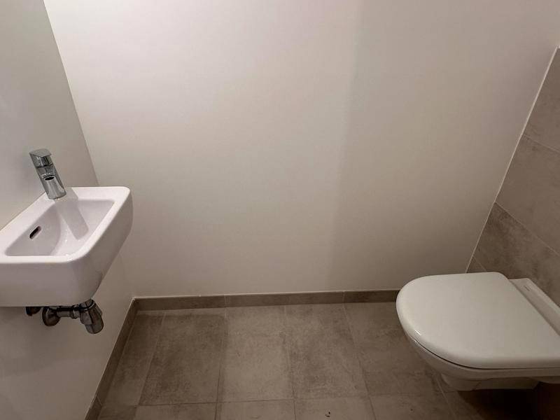 Gäste-WC mit wandhängender Toilette und kleinem Waschbecken, ausgestattet mit modernen Fliesen.