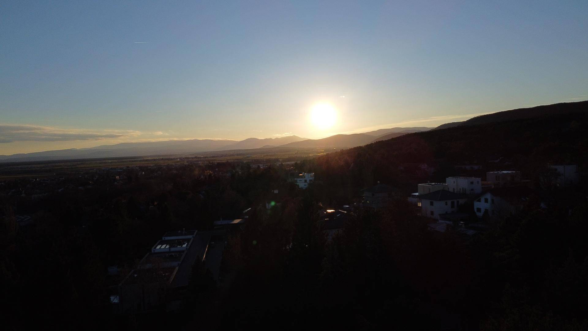 Malerischer Sonnenuntergang über einer weiten Landschaft mit entfernten Bergen und Siedlungsgebieten.