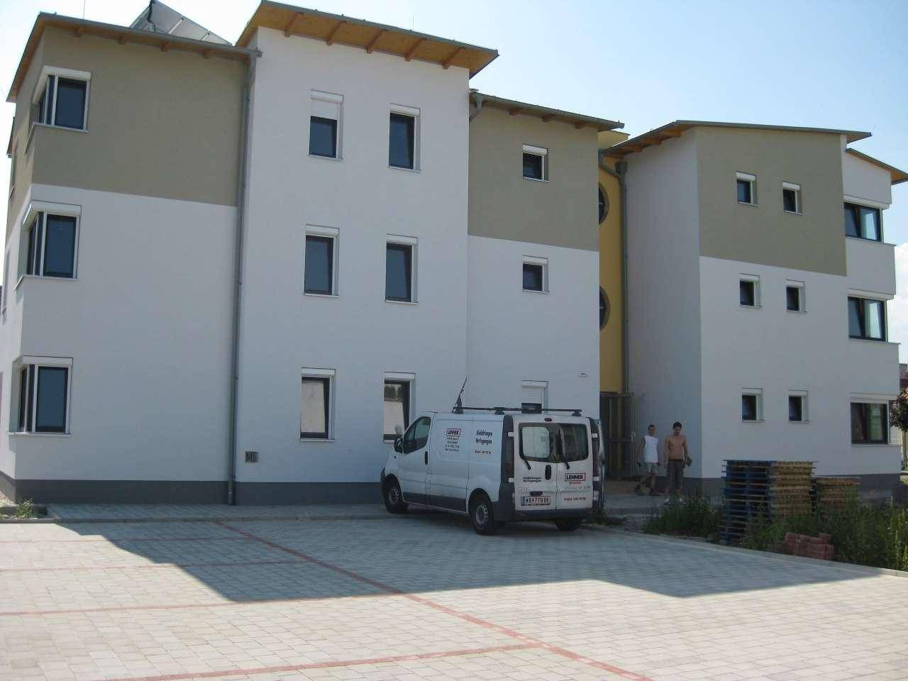 Rückansicht des modernen Wohngebäudes mit gepflastertem Parkplatz und Lieferwagen.