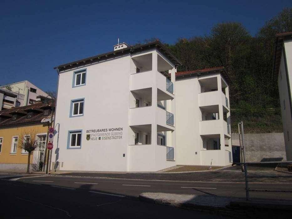 Weißes Apartmentgebäude mit blauen Fensterrahmen und Balkonen, gekennzeichnet als betreubares Wohnen.