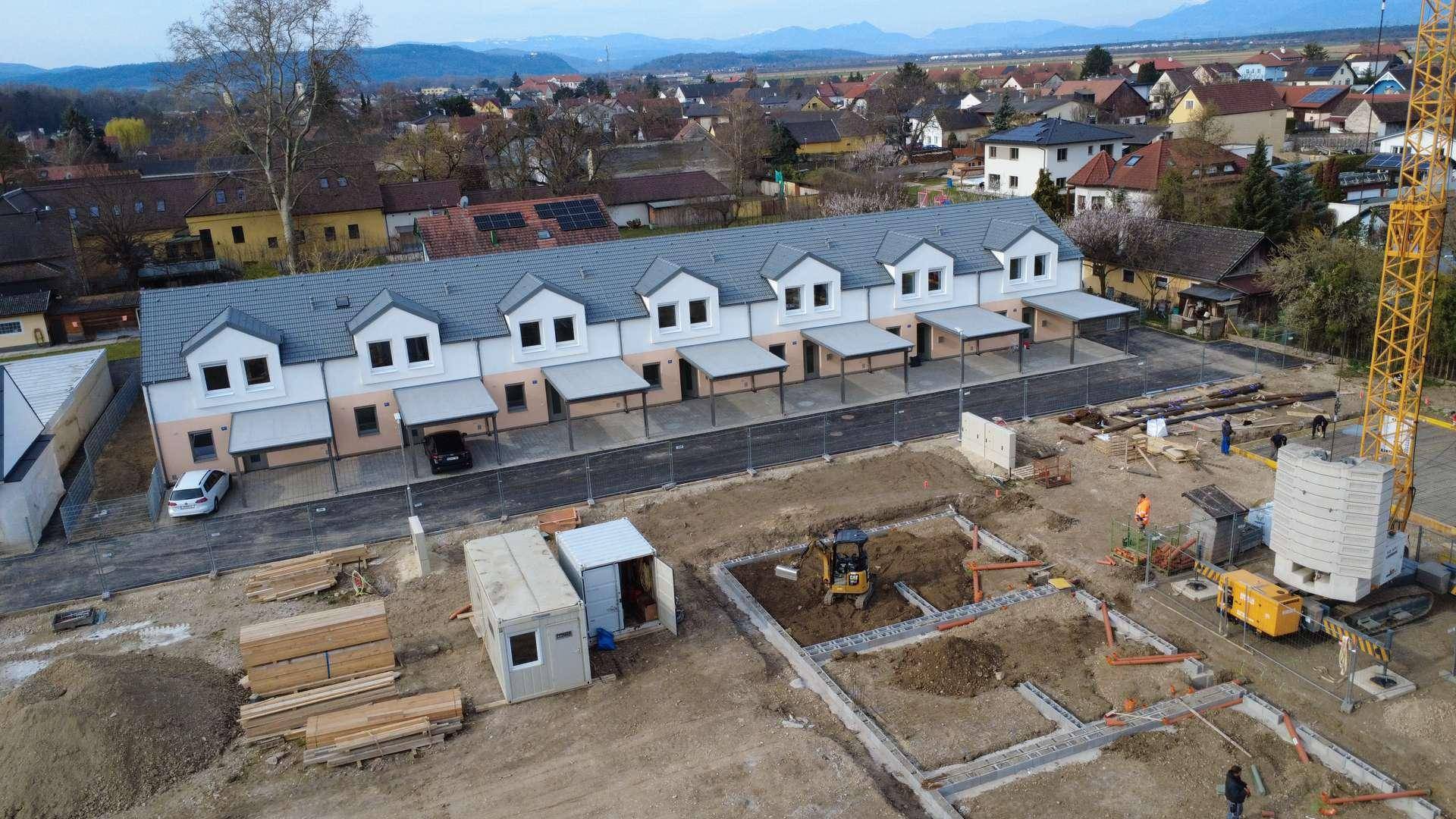 Weitläufige Luftaufnahme einer Reihenhaussiedlung im Bau mit Carports und Kran.