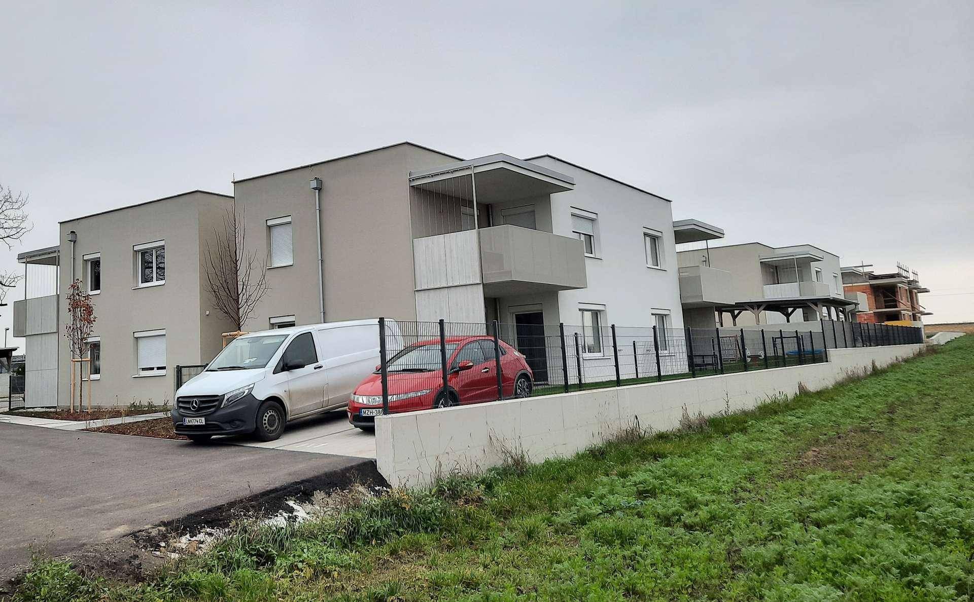 Moderne Wohngebäude mit hellen Fassaden und Balkonen, umgeben von einer Grünfläche unter bewölktem Himmel.