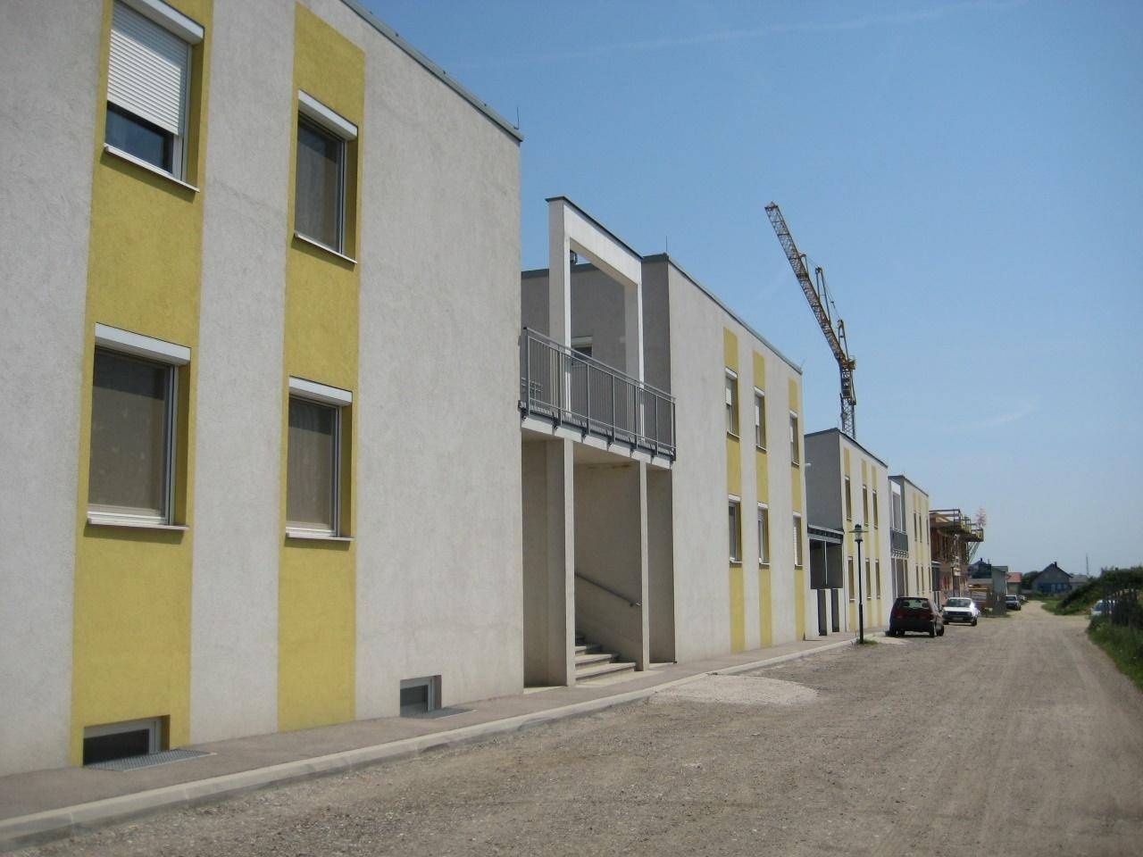 Reihe moderner Wohngebäude mit gelb-weißen Fassaden entlang einer Straße, mit einem Baukran im Hintergrund.