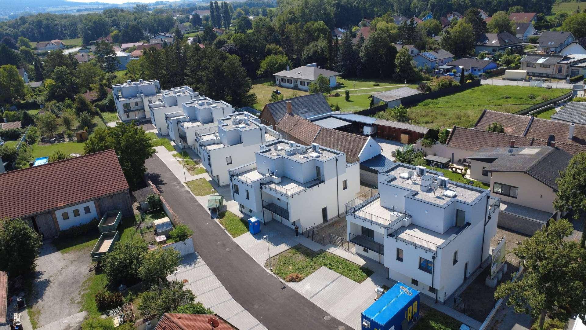 Luftaufnahme einer neuen Wohnsiedlung mit modernen Reihenhäusern, Straße und Grünflächen in ländlicher Umgebung.