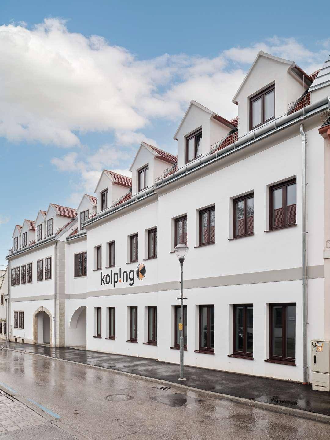 Modernes Gebäude mit weißer Fassade, Satteldach und Gaubenfenstern unter blauem Himmel.