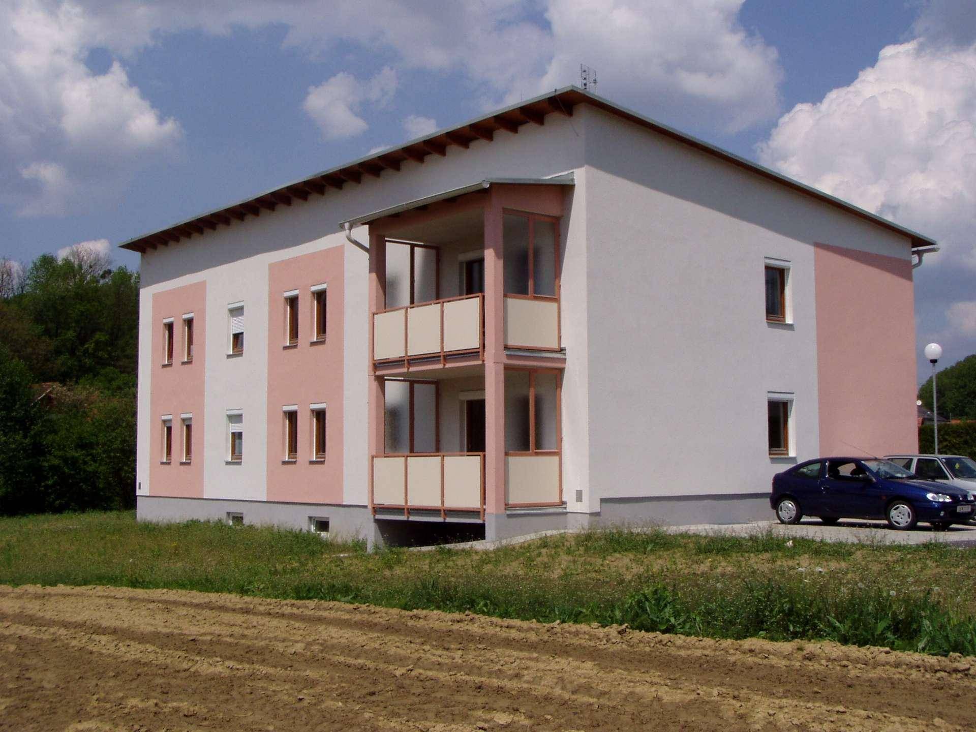 Neues Mehrfamilienhaus mit moderner Architektur, weiß-rosa Fassade, Balkonen und ländlichem Ausblick.