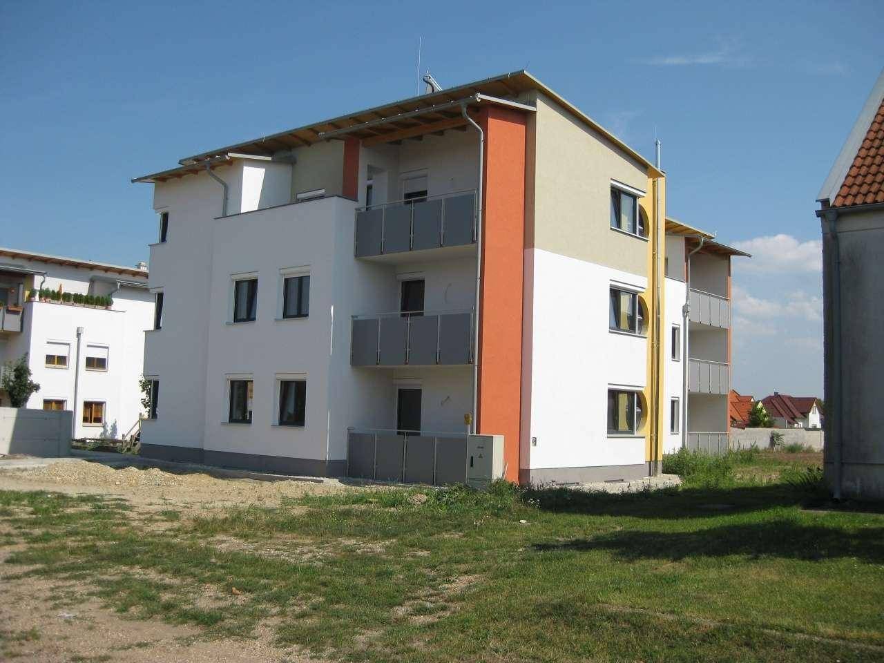 Seitenansicht eines modernen Wohngebäudes mit Balkonen und farbigen Akzenten an der Fassade.