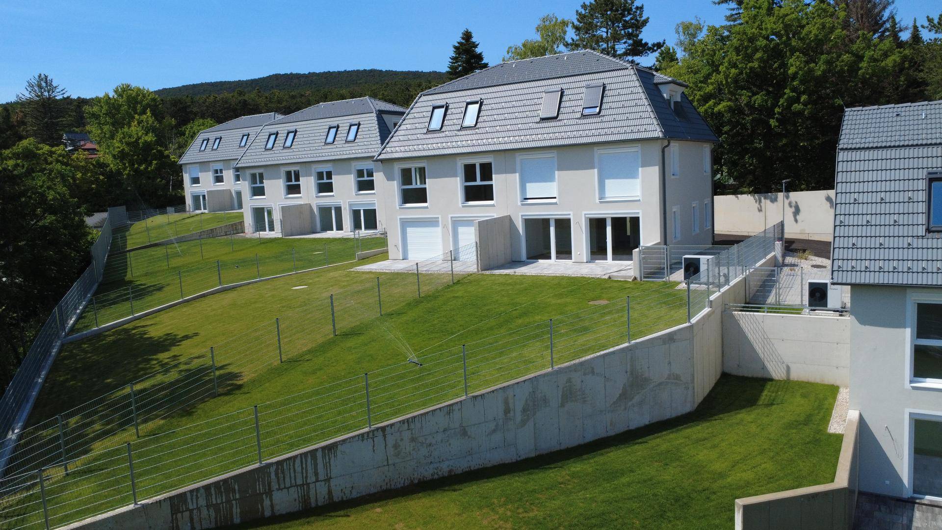 Eine Reihe von modernen Neubauhäusern mit großen Fenstern und Terrassen in einer grünen Umgebung.