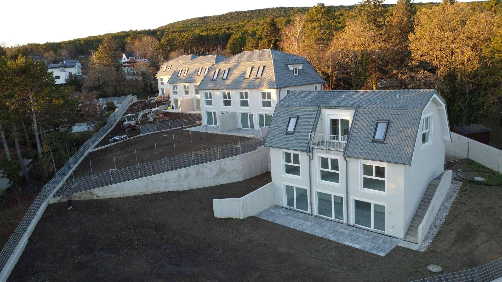 Reihe von modernen Doppelhaushälften in Bauphase mit vorbereiteten Gärten und Terrassen.