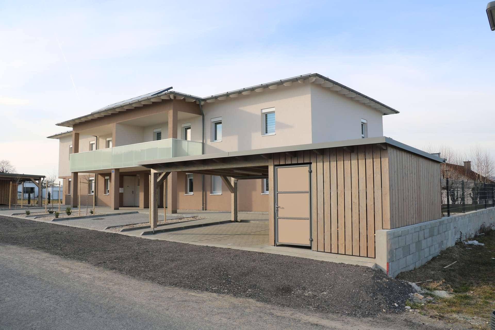 Modernes Wohngebäude mit Carports und Abstellraum unter klarem Himmel.
