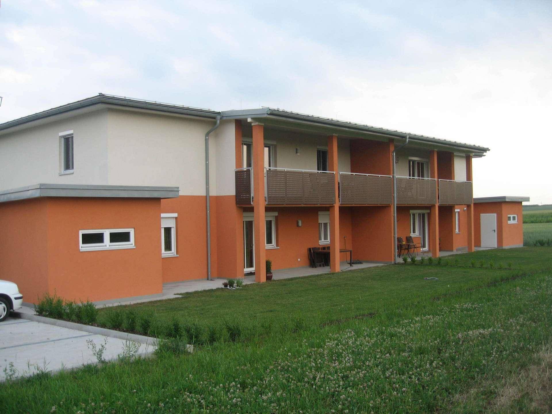 Modernes Mehrfamilienhaus mit orangefarbener Fassade, Balkonen und großem Gartenbereich.