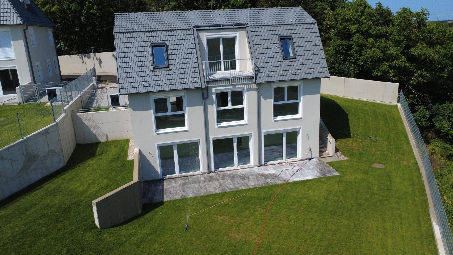Modernes Neubauhaus mit heller Fassade, großen Fensterfronten und einem kleinen Balkon im Dachgeschoss.