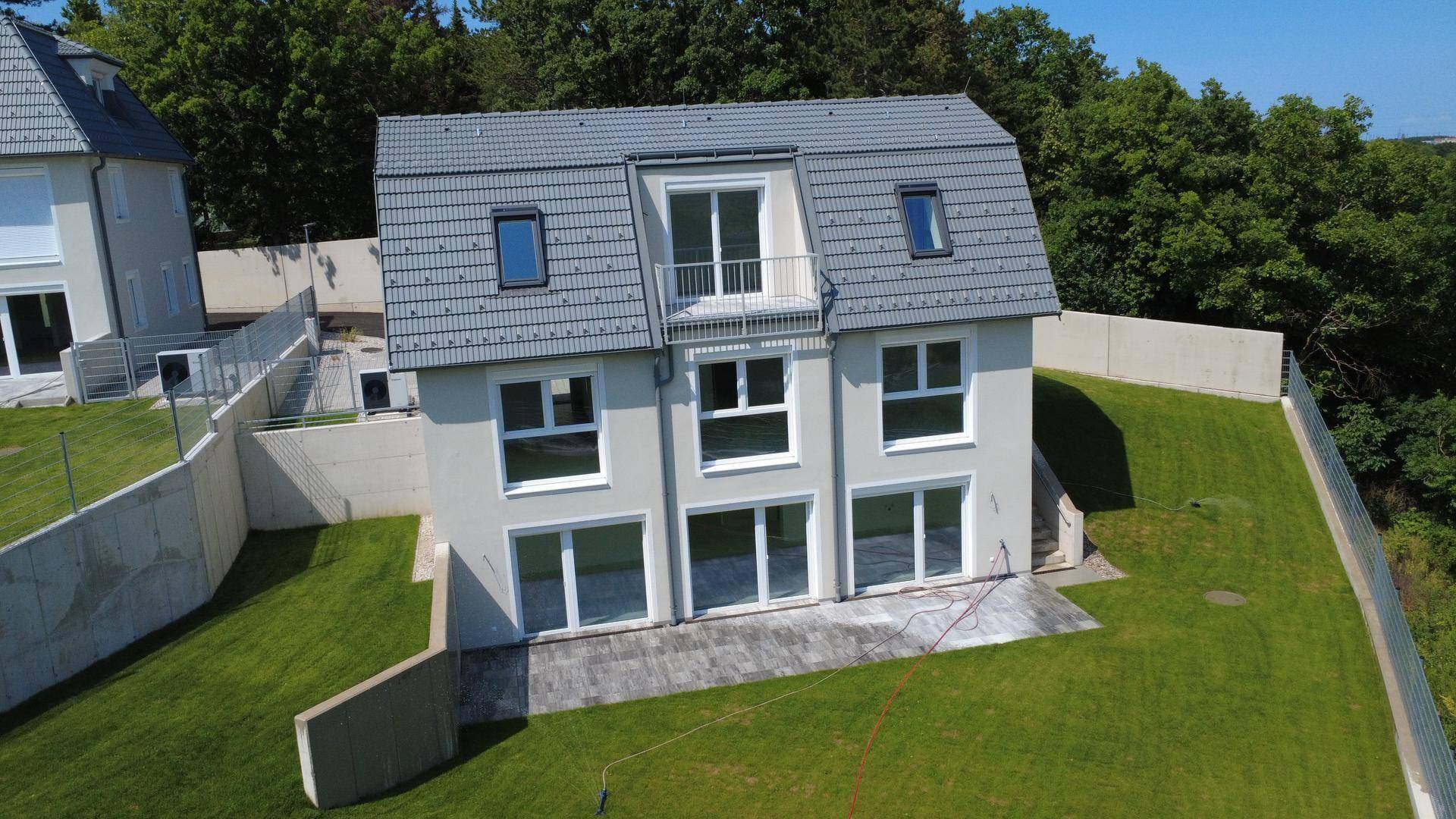Einzelnes Neubauhaus mit moderner Fassade, großen Fenstern und einem kleinen französischen Balkon.