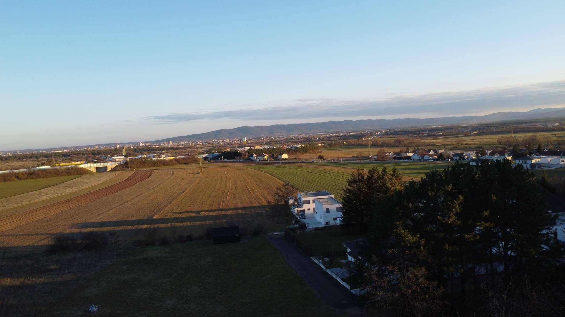 Weitläufige Landschaft mit Feldern und einem modernen Haus am Horizont bei klarem Himmel.
