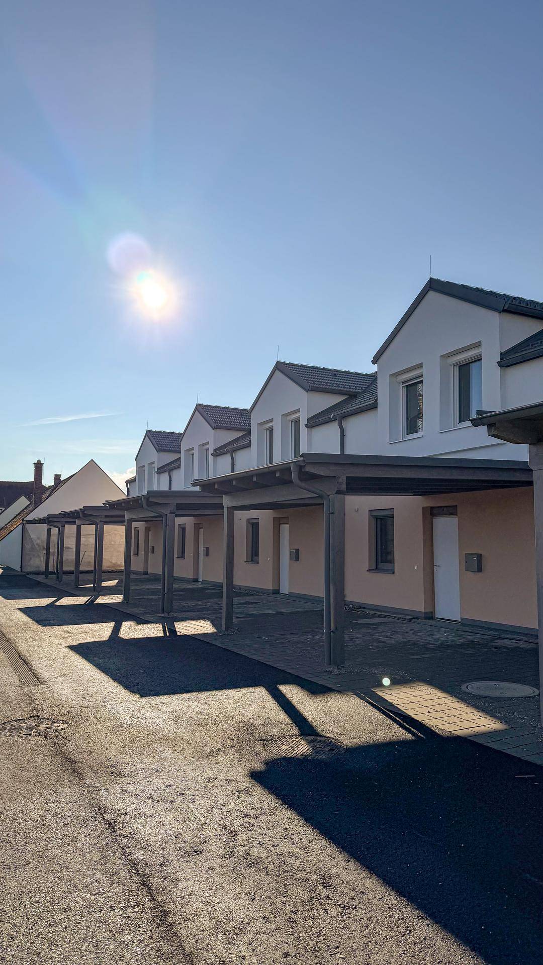 Reihe von modernen Neubauhäusern mit Carports unter strahlendem Sonnenschein.