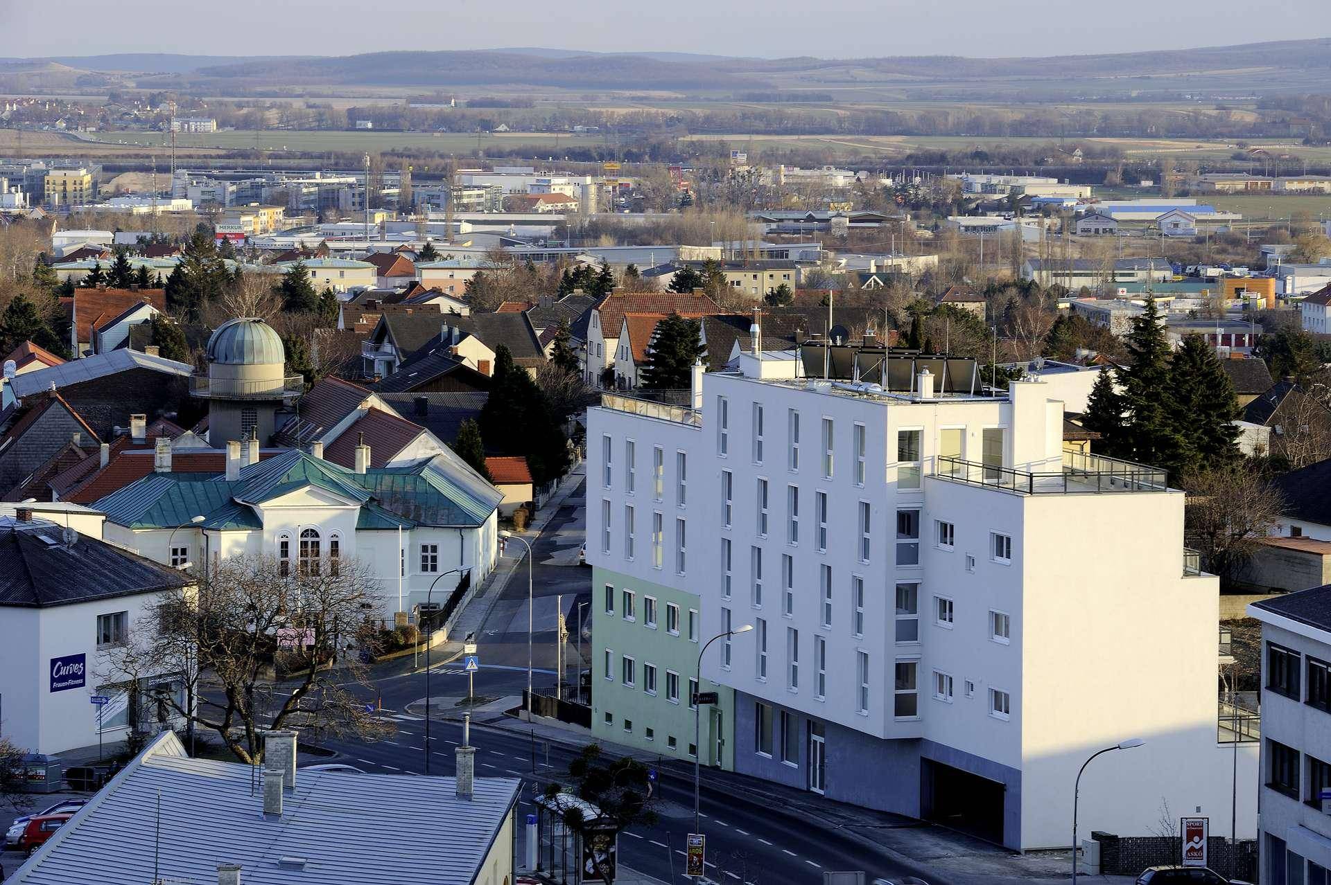 Panoramablick auf eine Stadt mit einem modernen Wohngebäude und umliegender Landschaft.