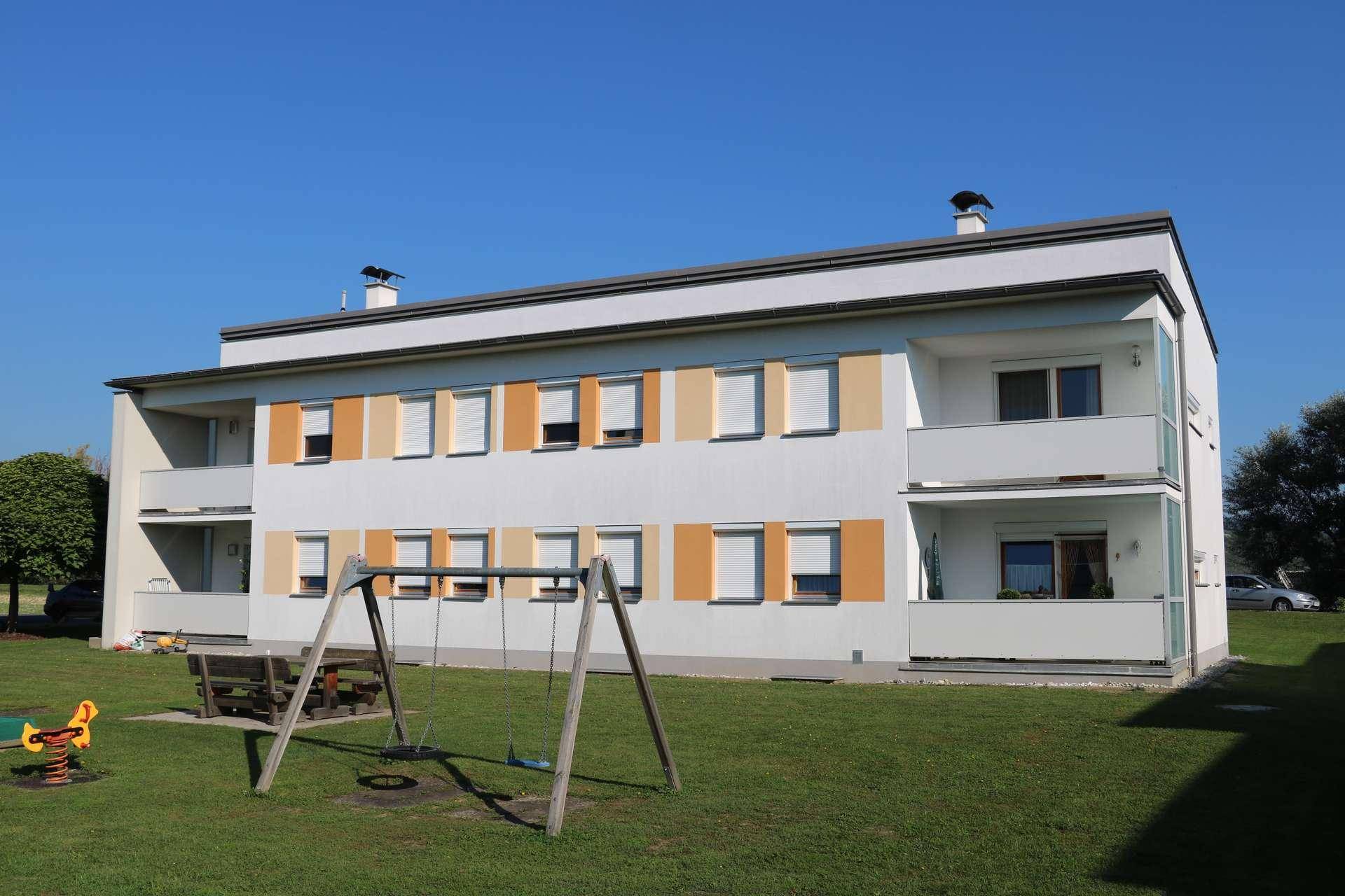 Modernes Wohngebäude mit Spielplatz im Vordergrund und farbigen Fensterakzenten.