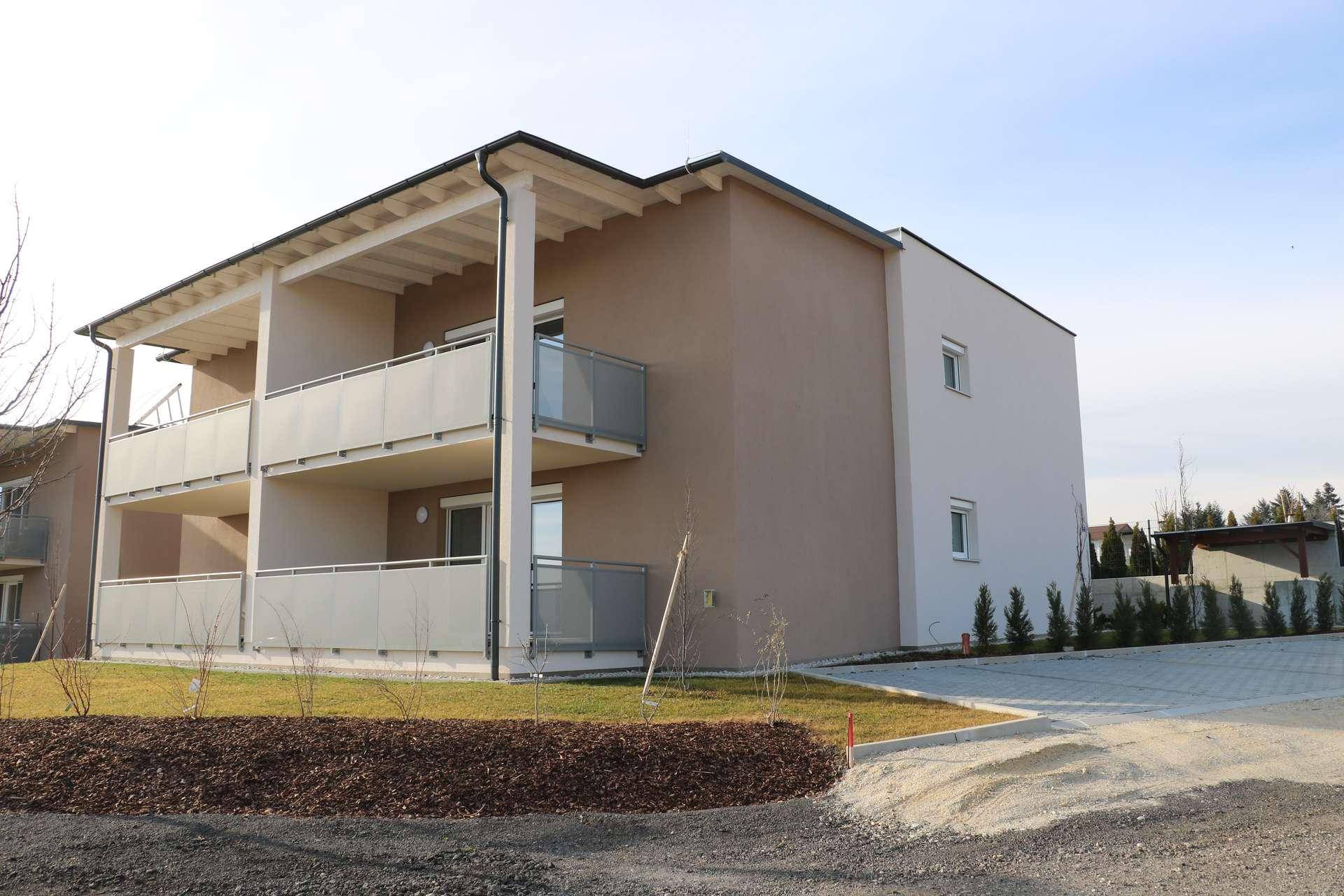 Modernes Apartmentgebäude von der Seite mit Balkonen und frisch angelegten Außenbereichen.