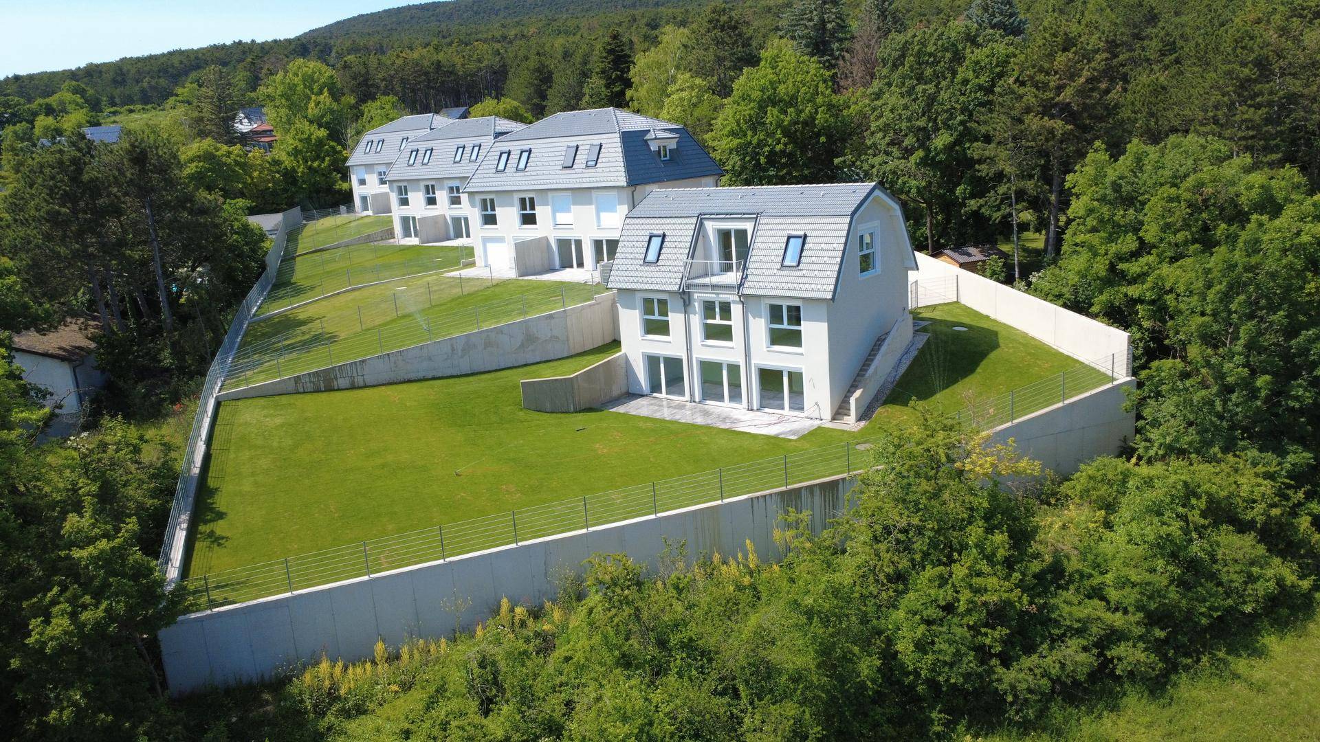 Panoramablick auf eine Reihe von Neubauten mit gepflegten Gärten und umgebender Natur.