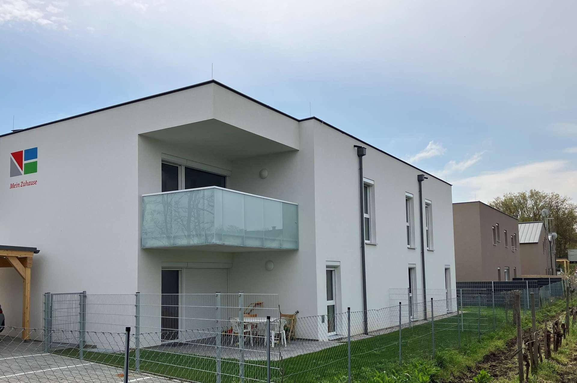 Modernes weißes Gebäude mit Balkon, möblierter Terrasse und gepflegtem Rasenbereich.