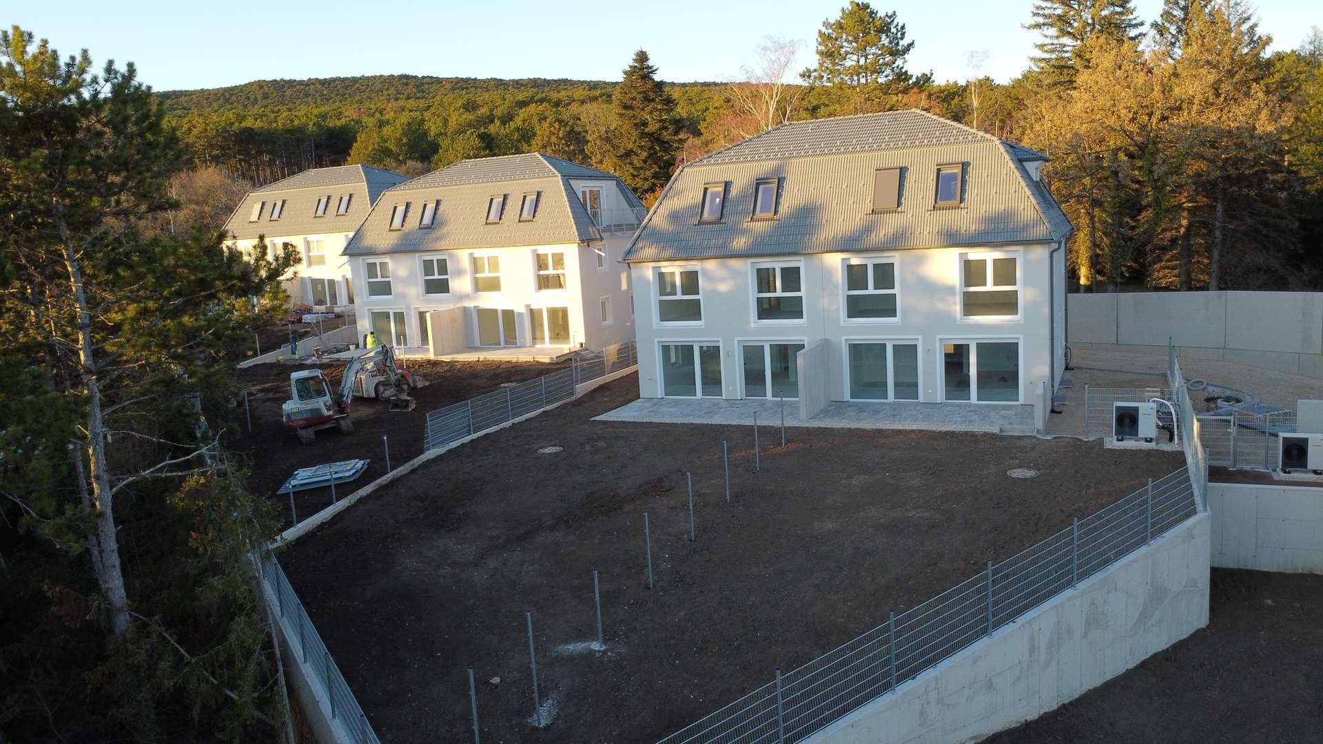 Reihe von modernen Doppelhaushälften in Bauphase mit vorbereiteten Gärten und Terrassen.