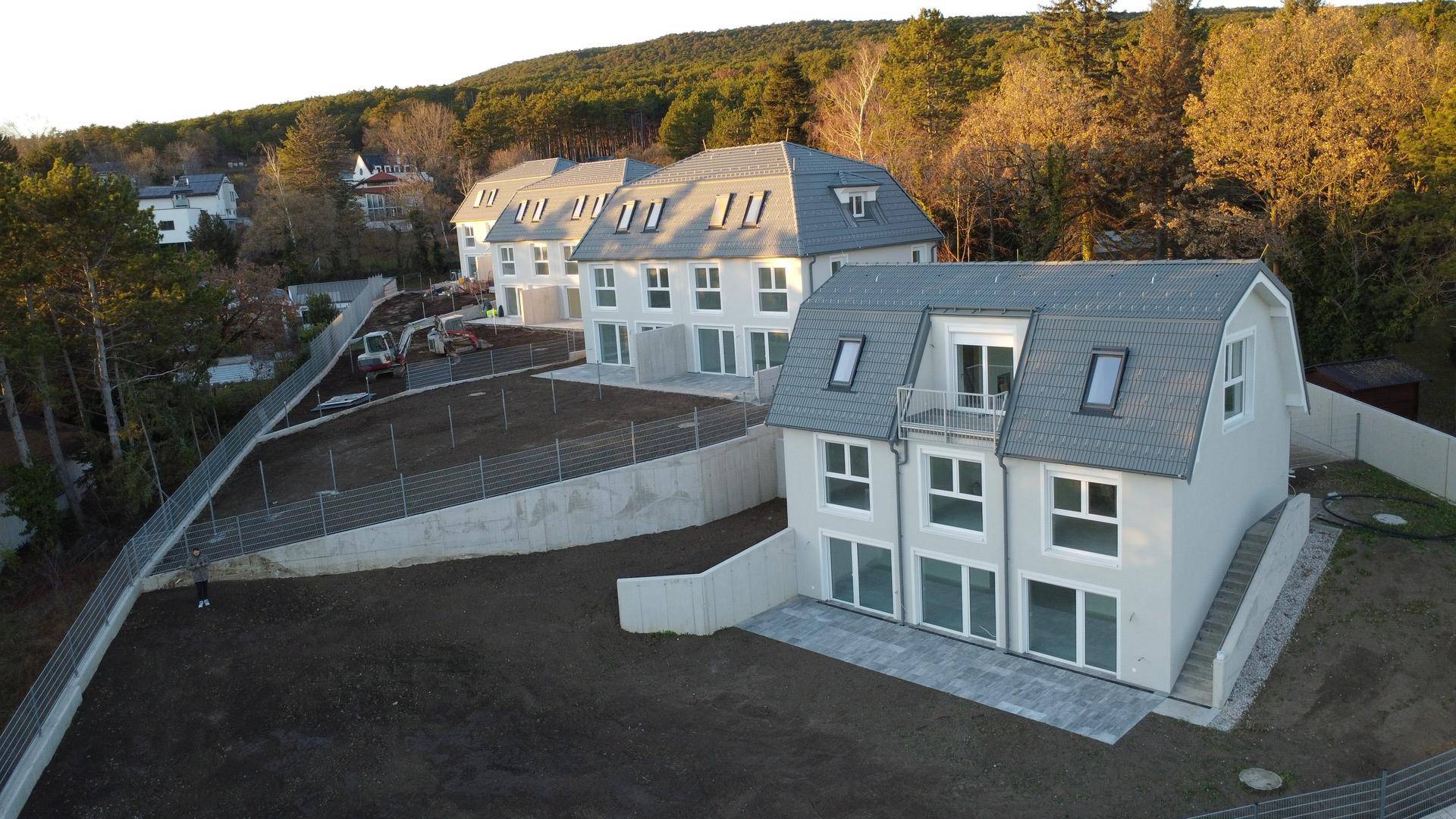 Neubau-Reihenhäuser in Hanglage mit Terrassen und Balkonen, umgeben von Wald und Natur.