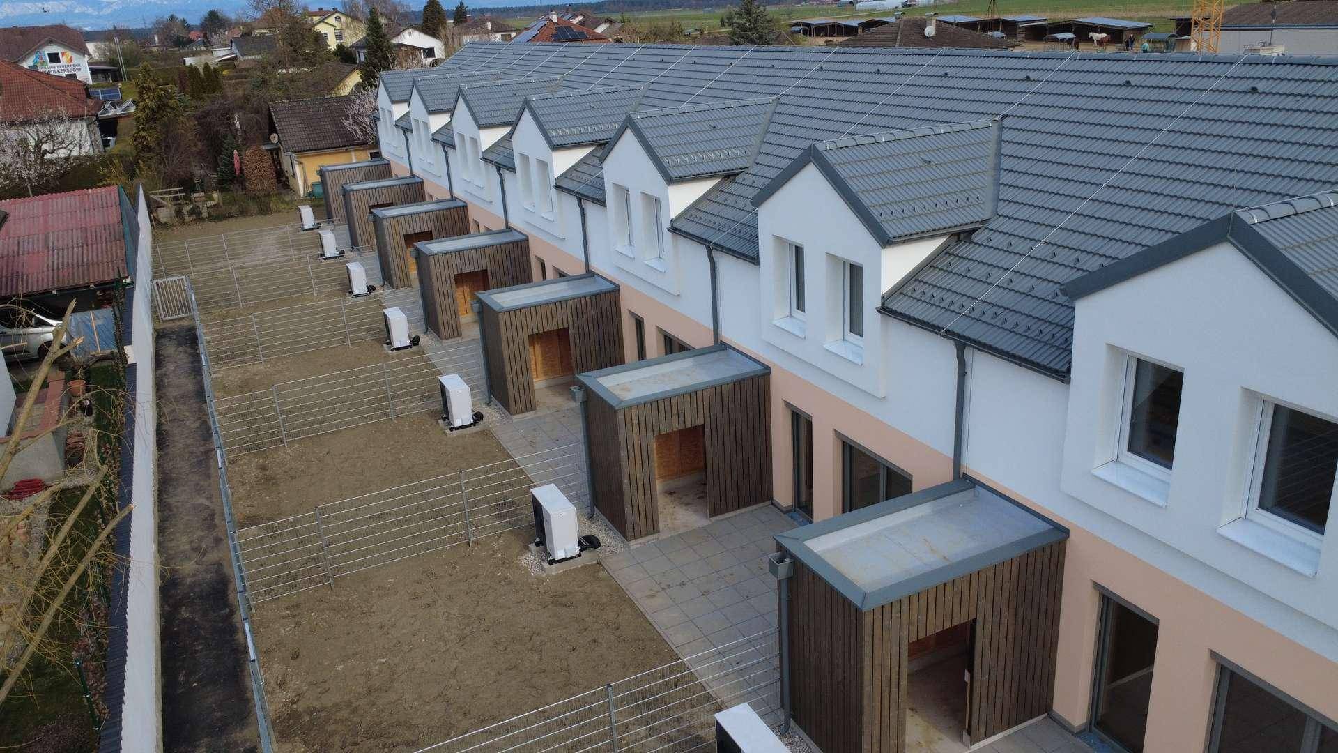 Rückseite einer Reihenhauszeile mit kleinen Terrassen, Gärten und Wärmepumpen.