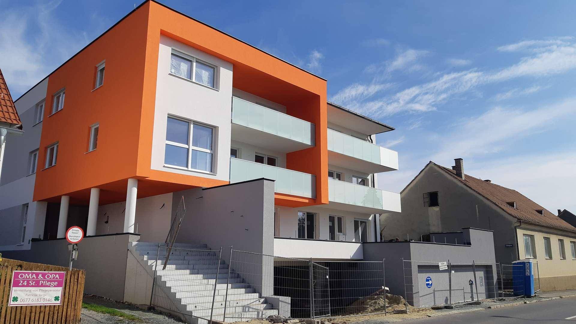 Neues Wohngebäude mit markanter orange-weißer Fassade und Balkonen, umgeben von Baustellenabsperrungen.