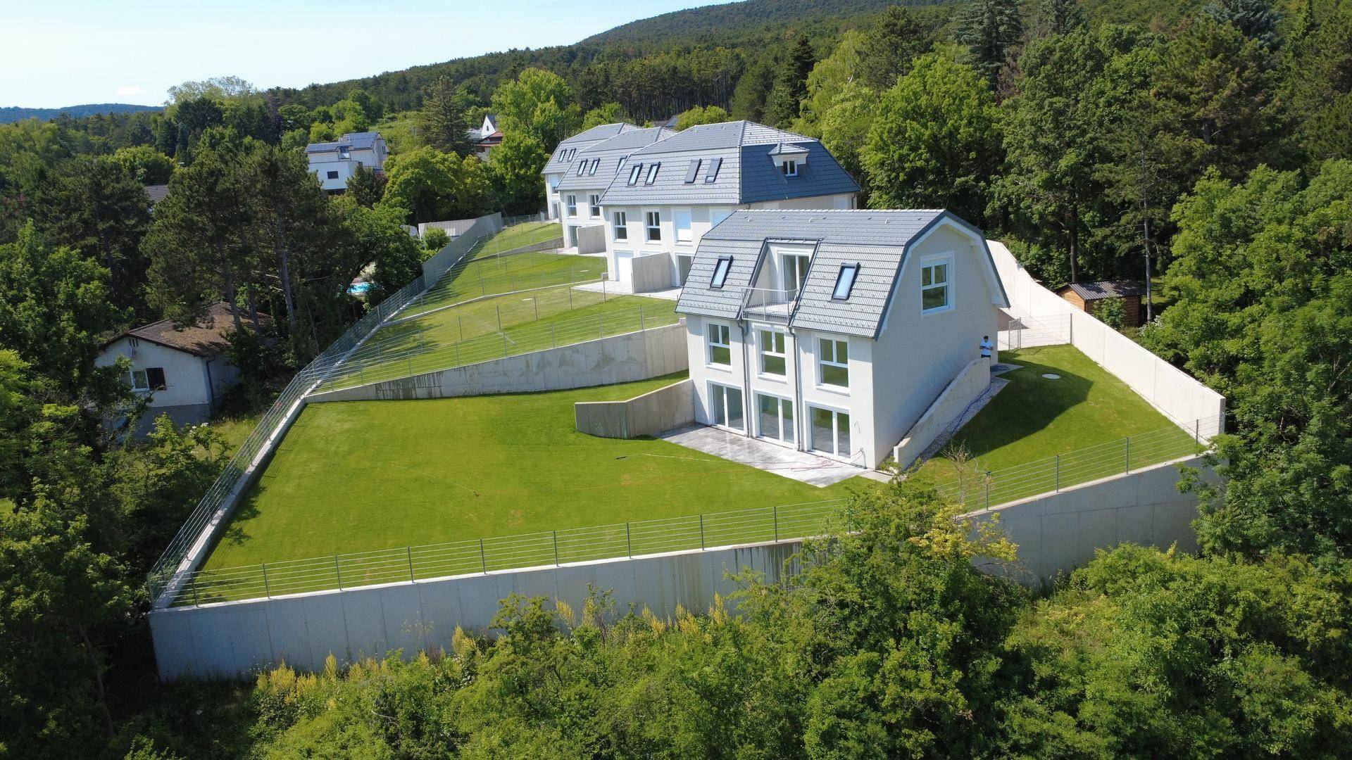 Neubau-Reihenhäuser in Hanglage mit frisch angelegten Rasenflächen und moderner Architektur, umgeben von Wald.