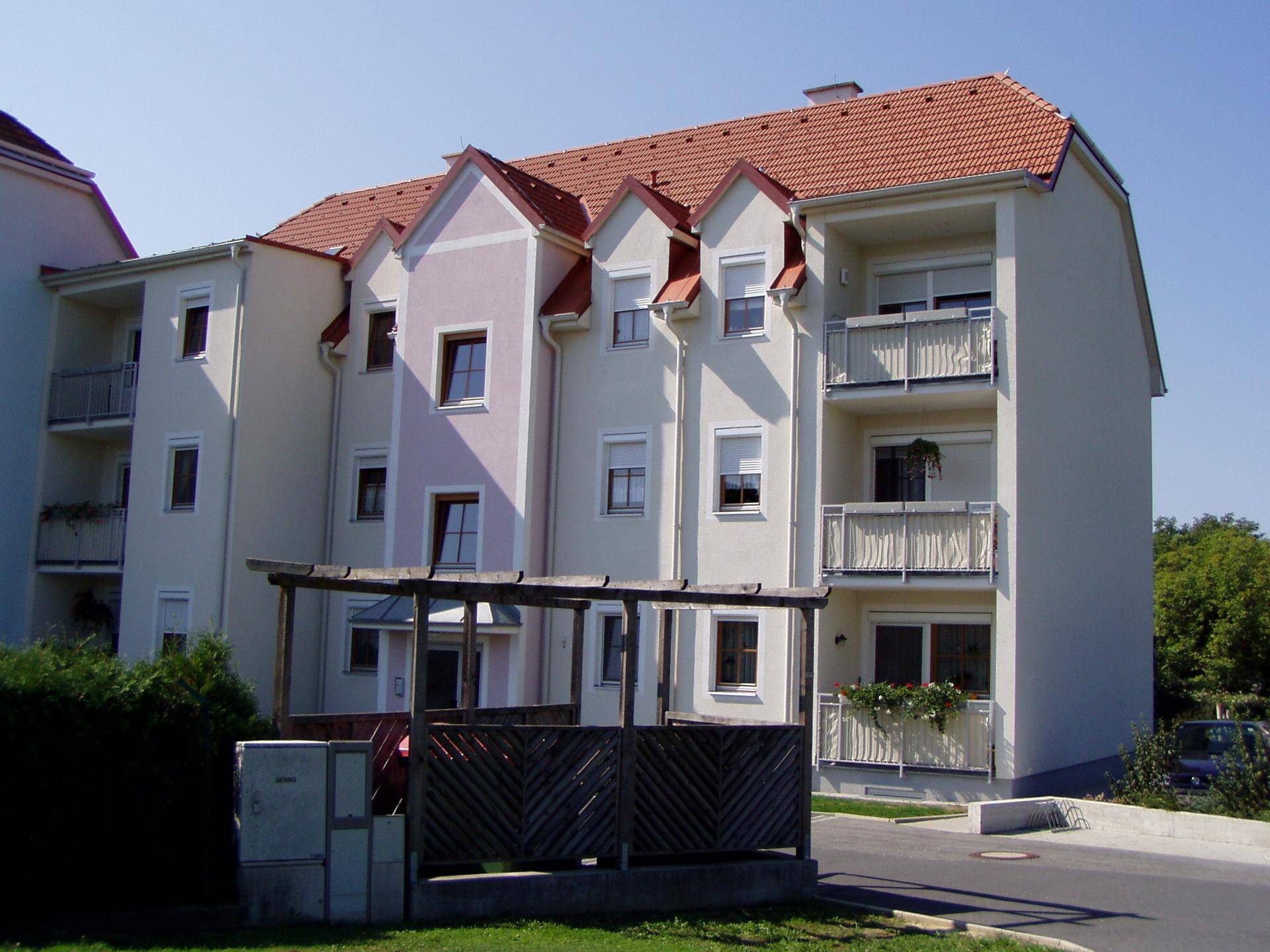 Mehrfamilienhaus mit heller Putzfassade, roten Ziegeldächern und mehreren Balkonen in gepflegter Umgebung.