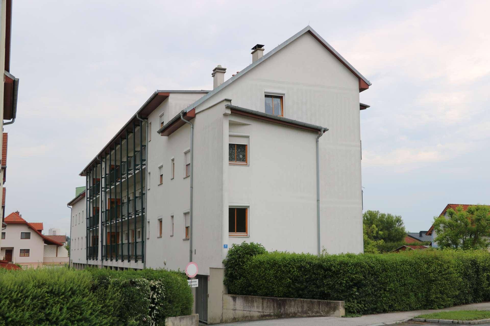 Modernes Wohngebäude mit weißer Fassade, großen Fenstern und einer grünen Hecke im Vordergrund.