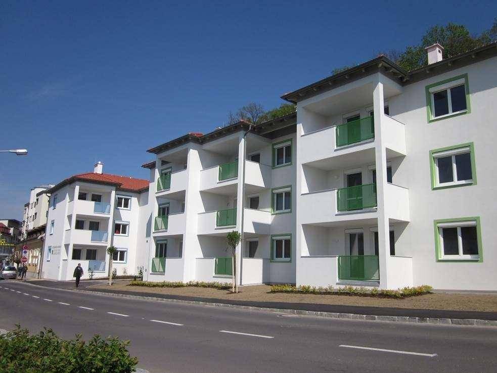Moderne Apartmentgebäude mit weißer Fassade und grünen Balkonen entlang einer Straße unter blauem Himmel.