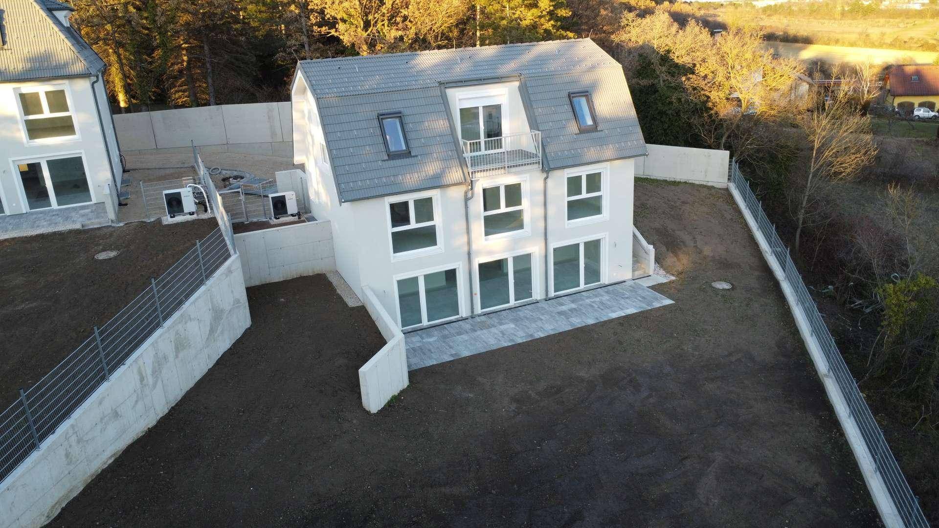 Neubau-Doppelhaushälfte mit frisch angelegtem Garten und moderner Architektur bei Sonnenuntergang.