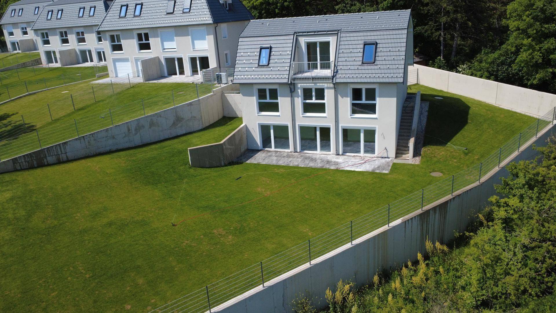 Moderne Reihenhäuser in Hanglage mit großen Fenstern und gepflegten Rasenflächen, umgeben von Natur.