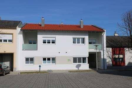 Wohngebäude mit rotem Satteldach, weißer Fassade und kleinen Balkonen.